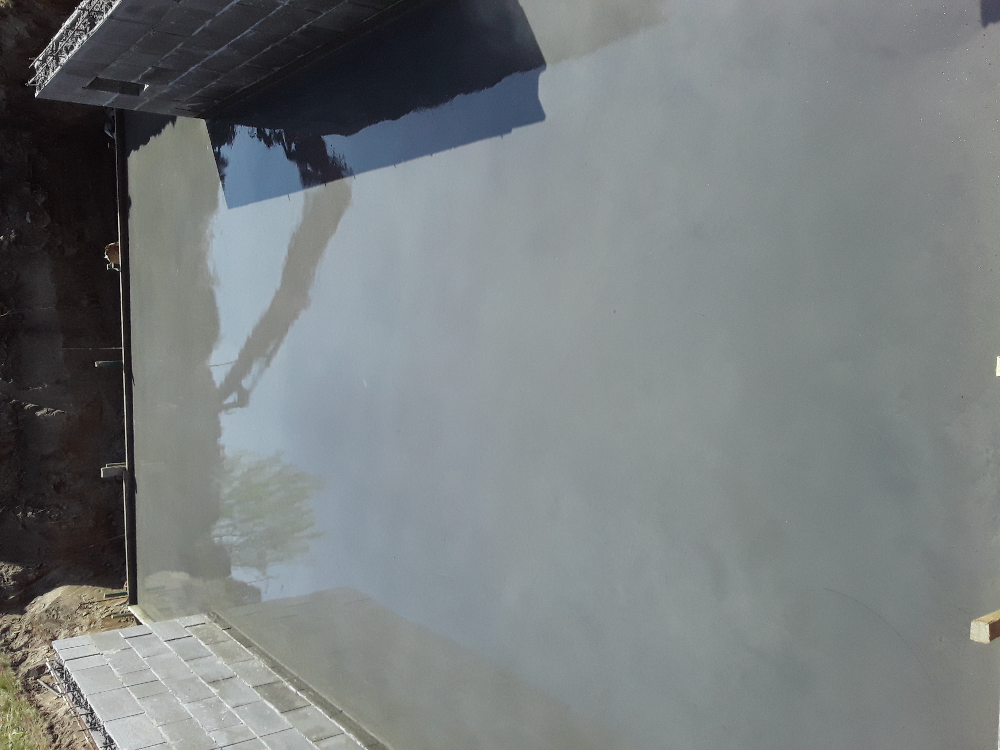 Świeżo wylana, gładka, szara posadzka w trakcie realizacji, widoczne szalunki i zbrojenie w tle.