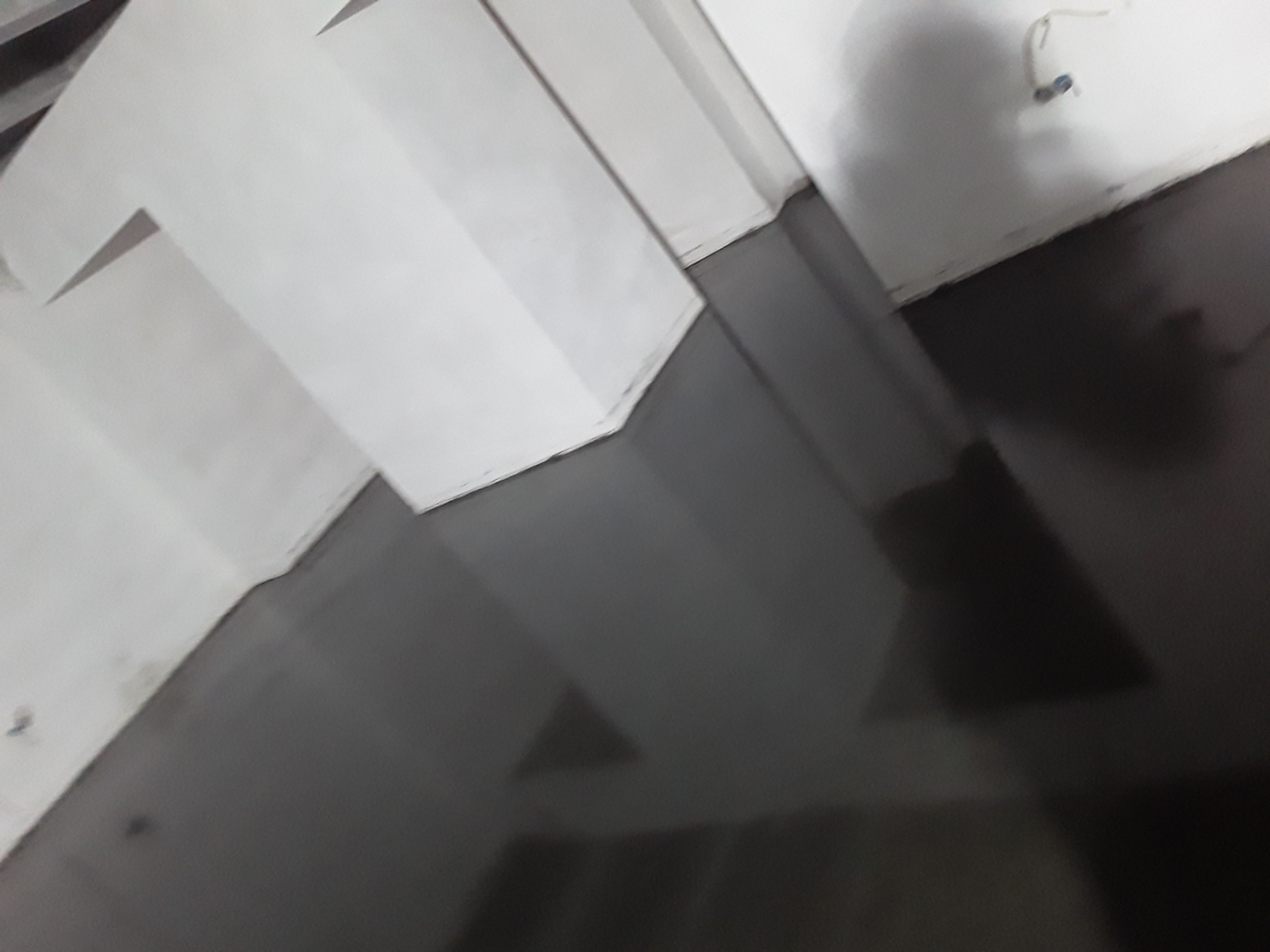 Świeżo wylana, ciemnoszara posadzka w pomieszczeniu z białymi ścianami; widoczne ślady po narzędziach i refleksy światła na gładkiej powierzchni.