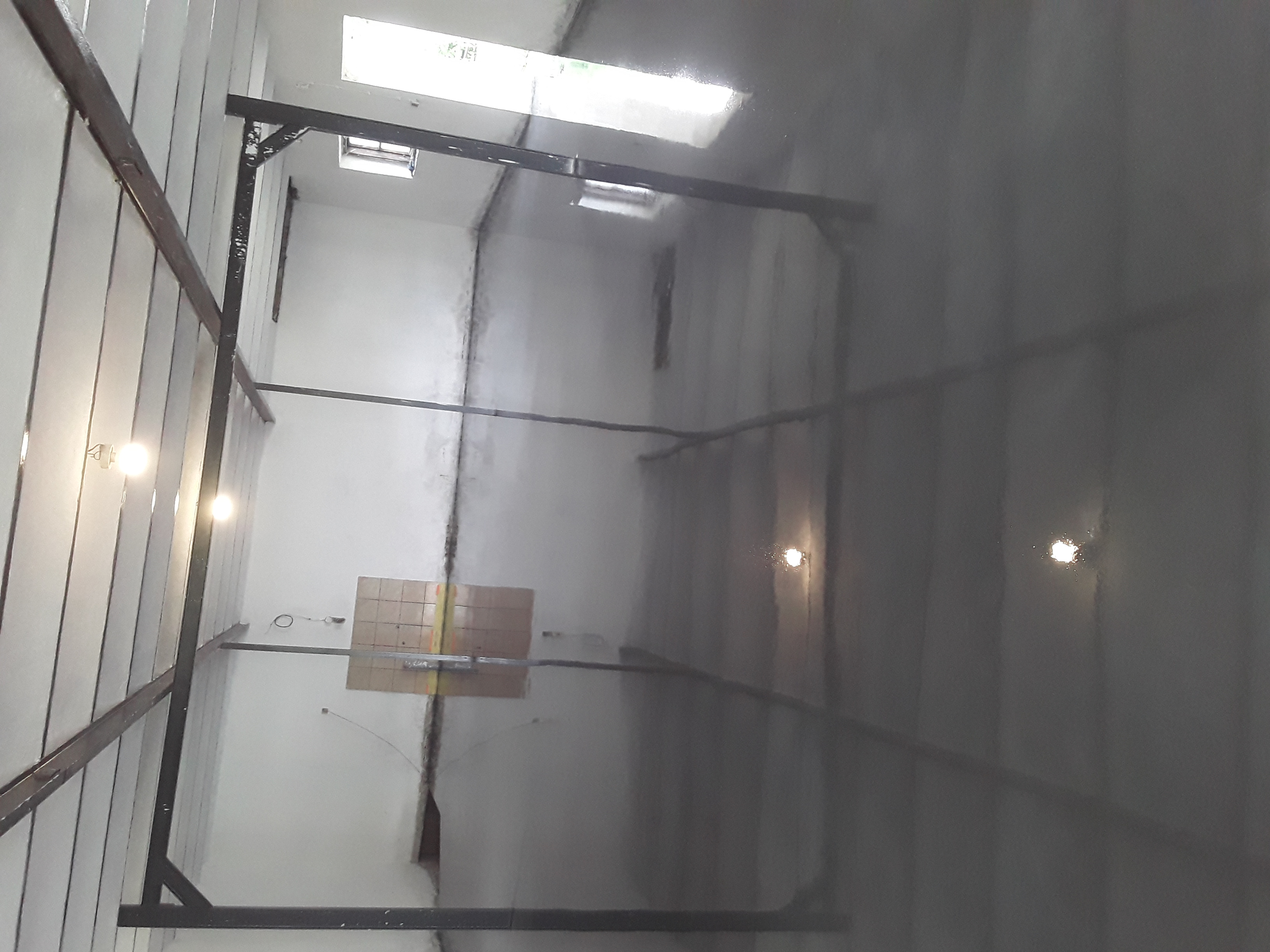 Świeżo wylana, błyszcząca, szara posadzka w hali przemysłowej, widoczne metalowe elementy konstrukcyjne pod sufitem i okna w tle.