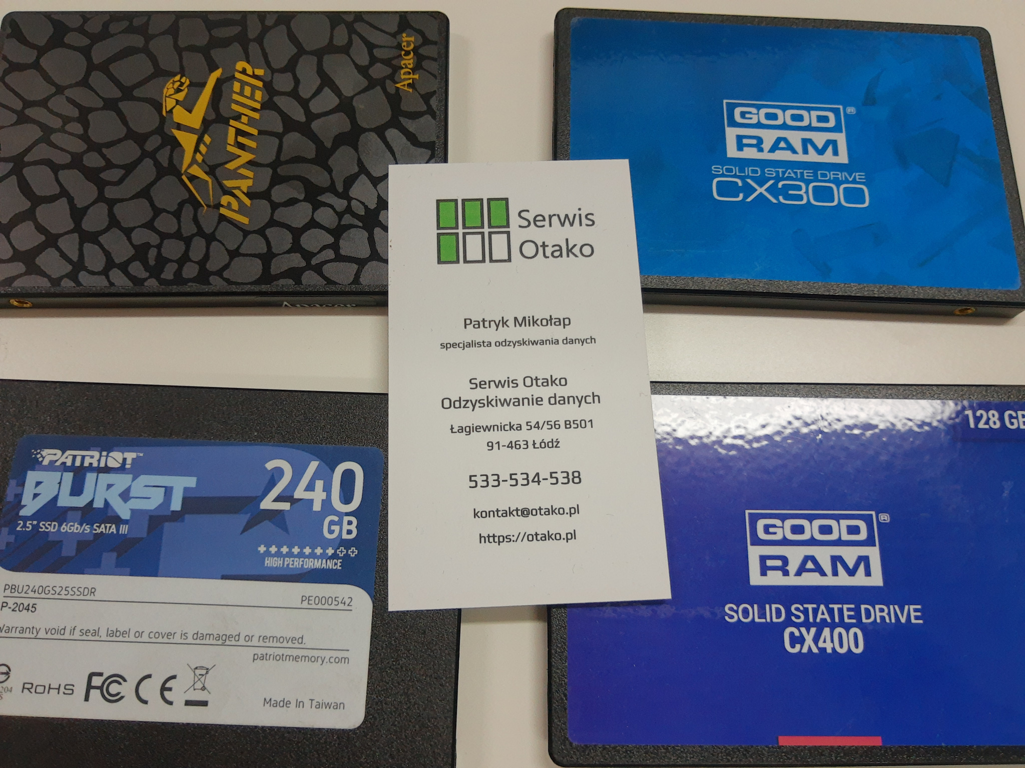 Dyski SSD różnych producentów (Apacer Panther, Patriot Burst, GoodRam CX300 i CX400) ułożone obok wizytówki firmy Serwis Otako, specjalizującej się w odzyskiwaniu danych.