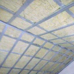 Skośna konstrukcja poddasza z metalowych profili wypełniona wełną mineralną, widok z dołu, w tle fragment ściany.