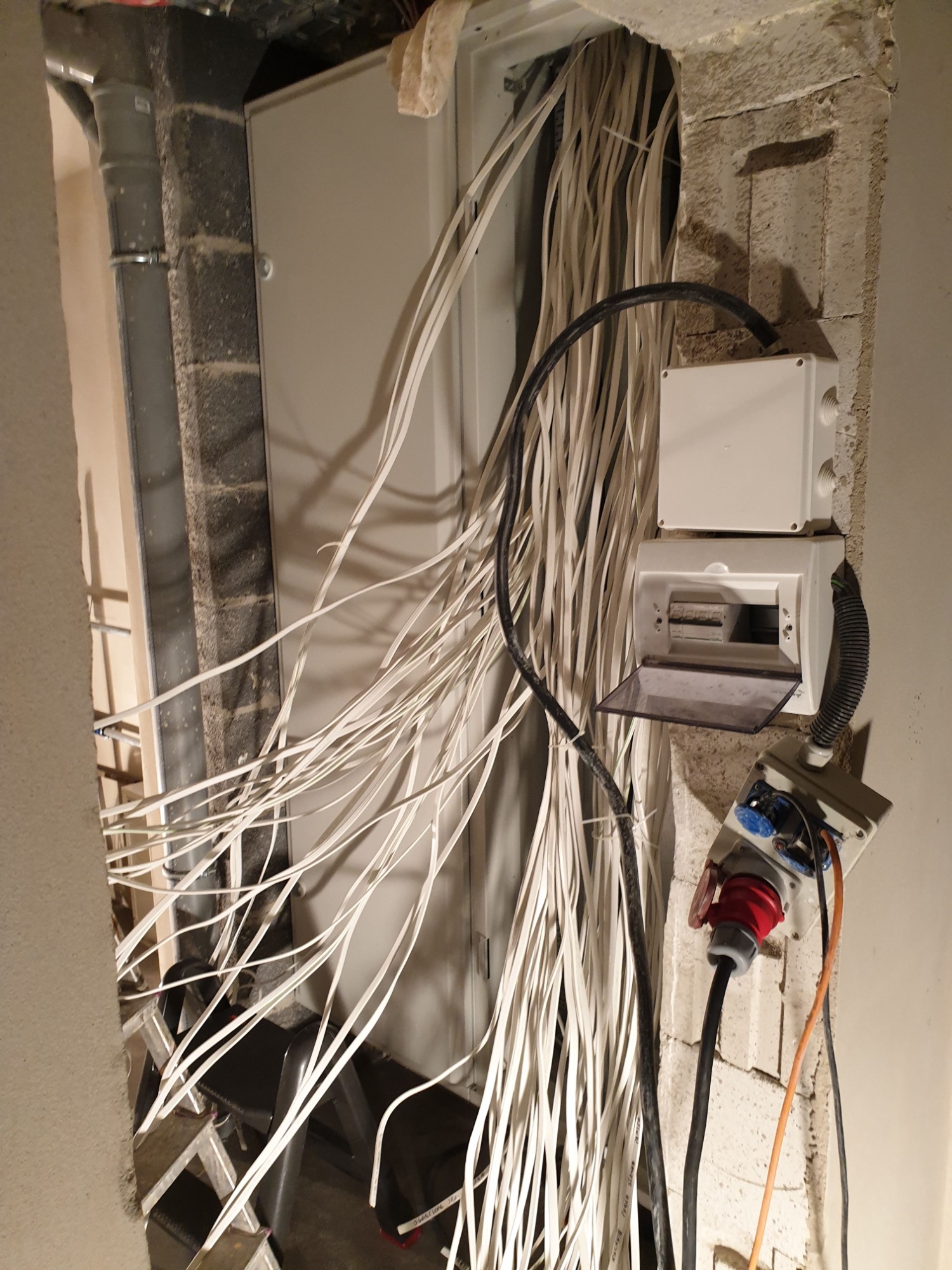 Rozdzielnia elektryczna w trakcie montażu w surowym wnętrzu, widoczne liczne przewody, puszki instalacyjne i gniazda siłowe na tle ceglastej ściany.