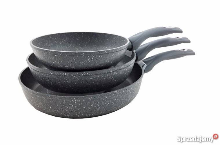 Zestaw trzech patelni granitowych ułożonych jedna na drugiej, z szarymi rączkami, na białym tle.