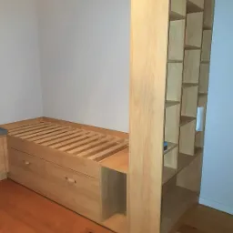 Drewniana antresola z wbudowanym łóżkiem i regałem na książki, widoczne szuflady pod łóżkiem i oświetlenie sufitowe.