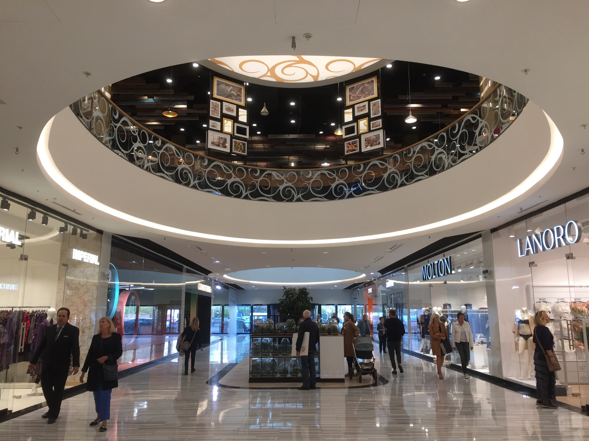 Wnętrze centrum handlowego z widokiem na antresolę z dekoracyjną balustradą i galerią zdjęć, widoczne sklepy Imperial, Molton i Lanoro.