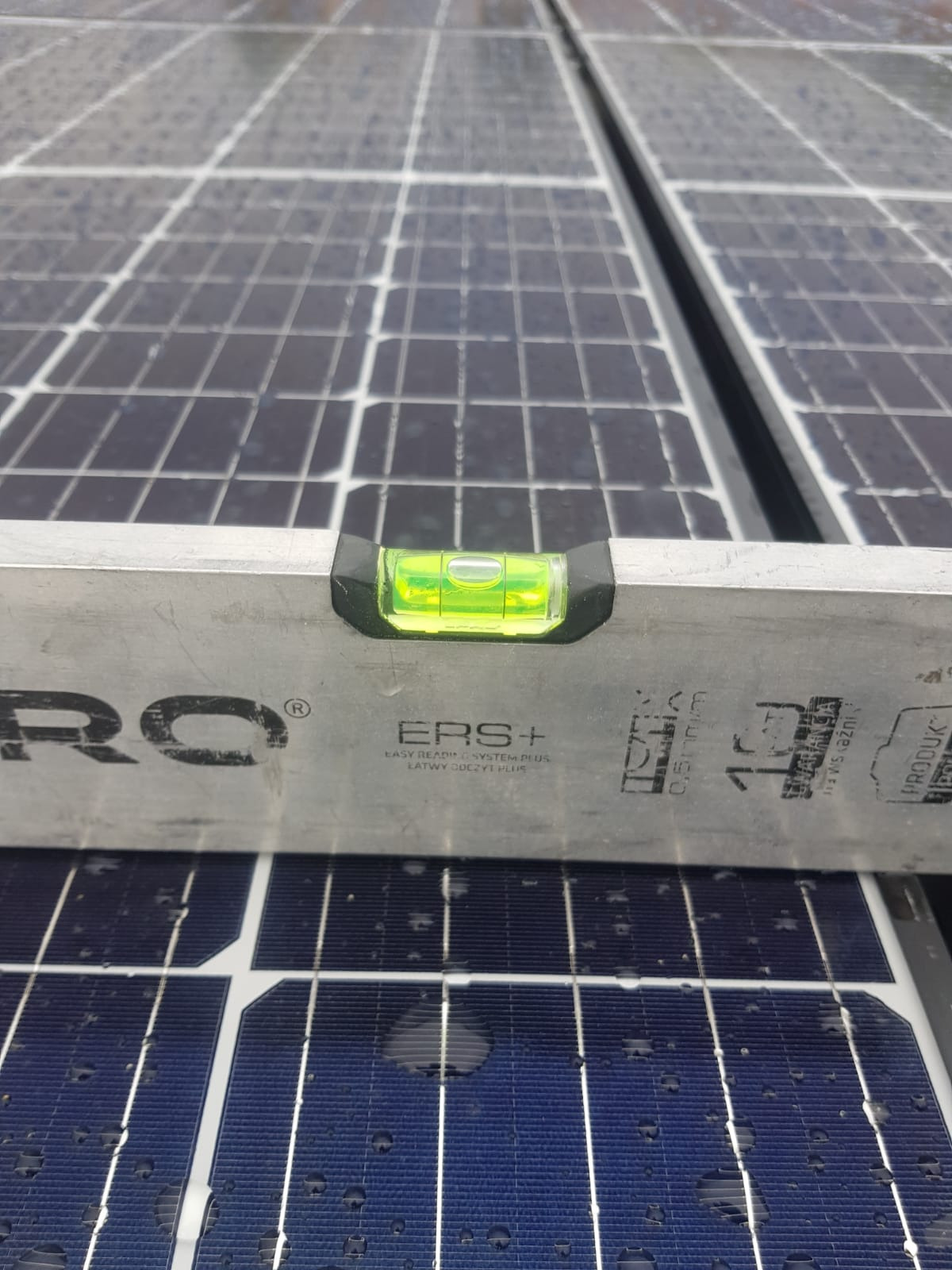 Poziomica na panelach słonecznych, sprawdzanie wypoziomowania instalacji, widoczne krople wody na panelach.