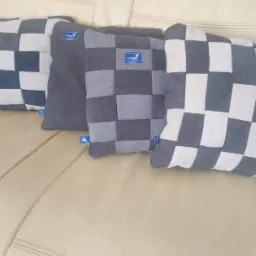 Cztery poduszki dekoracyjne w odcieniach szarości i bieli, ułożone na beżowej kanapie, z widocznymi metkami producenta.