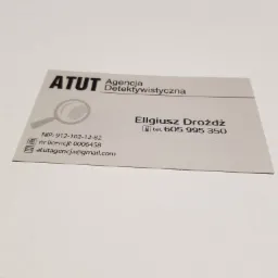 Wizytówka agencji detektywistycznej ATUT z lupą w logo, numerem NIP, licencją i adresem e-mail, należąca do Eligiusza Drożdża, z numerem telefonu 605 995 350.