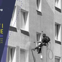 Pracownicy alpinistyczni czyszczący elewację budynku wielorodzinnego za pomocą myjki ciśnieniowej, widoczne liny i sprzęt asekuracyjny.