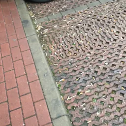 Zanieczyszczona kostka ażurowa i chodnik z czerwonej cegły przy samochodzie, zaśmiecone niedopałkami papierosów.