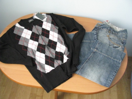 Czarny sweter w romby z metką i jasnoniebieskie dżinsy damskie na okrągłym drewnianym stole.