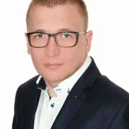 Portret ubezpieczyciela ze Żnina w okularach i granatowej marynarce na białym tle.