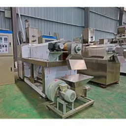 Kompleksowa linia produkcyjna z panelami sterowania i elementami ze stali nierdzewnej, umieszczona w hali przemysłowej z blachowanymi ścianami