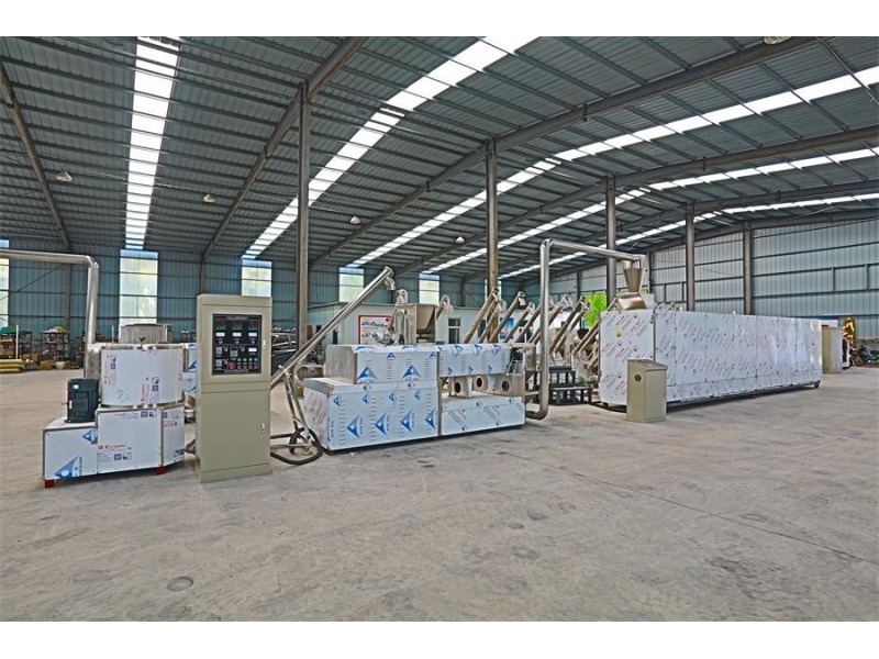 Widok hali produkcyjnej z zainstalowaną, dużą linią technologiczną, zabezpieczoną folią ochronną, z metalowymi rurami i szafą sterowniczą z wyświetlaczami.