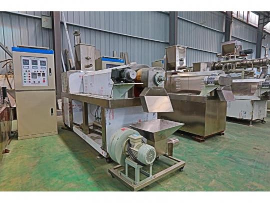 Kompleksowa linia produkcyjna z panelami sterowania i elementami ze stali nierdzewnej, umieszczona w hali przemysłowej z blachowanymi ścianami