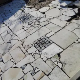 Ułożona nawierzchnia z nieregularnych płyt kamiennych z wkomponowanymi fragmentami kostki brukowej, w trakcie prac wykończeniowych.