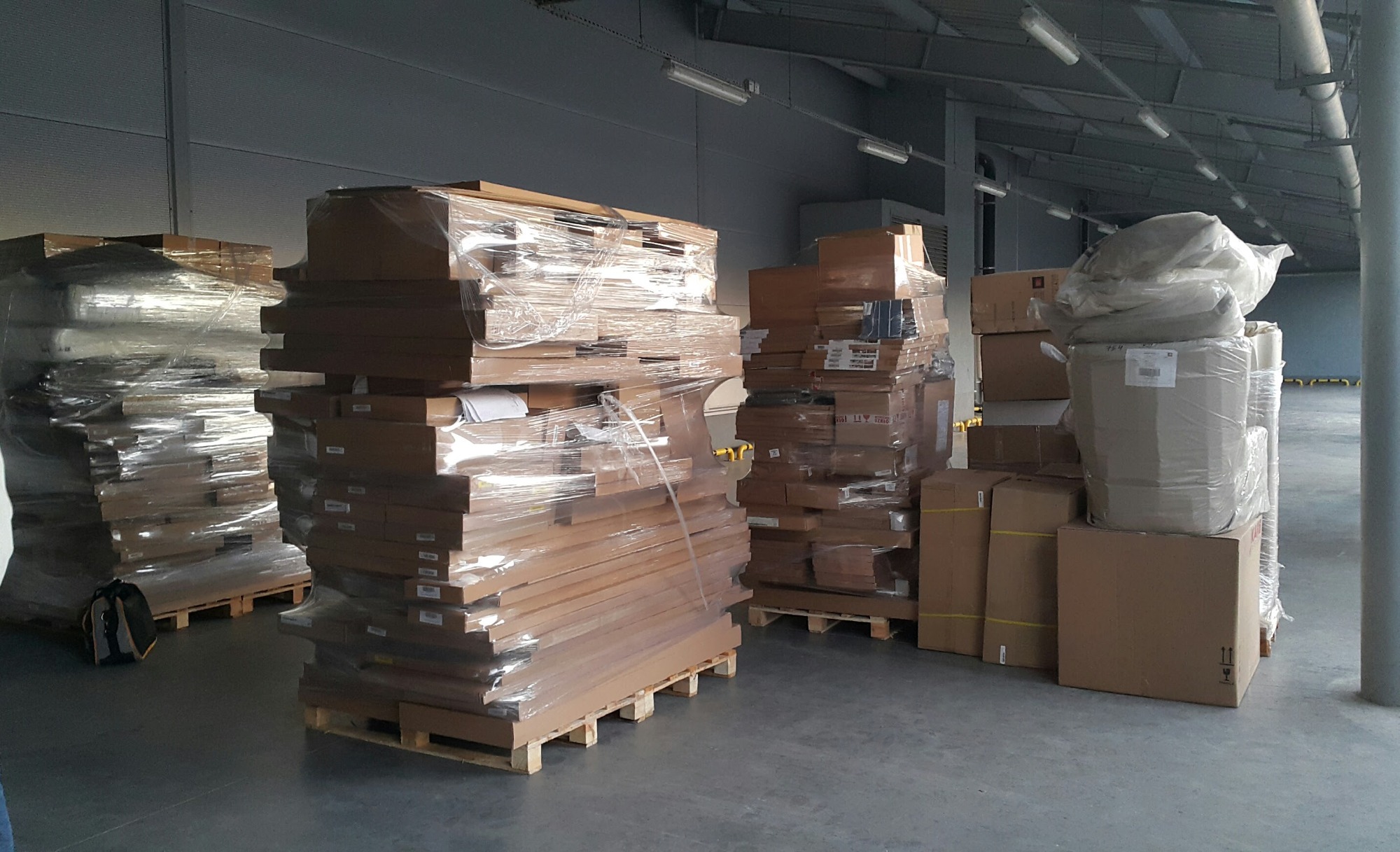 Spakowane elementy drewniane na paletach, zabezpieczone folią, w magazynie przed montażem.