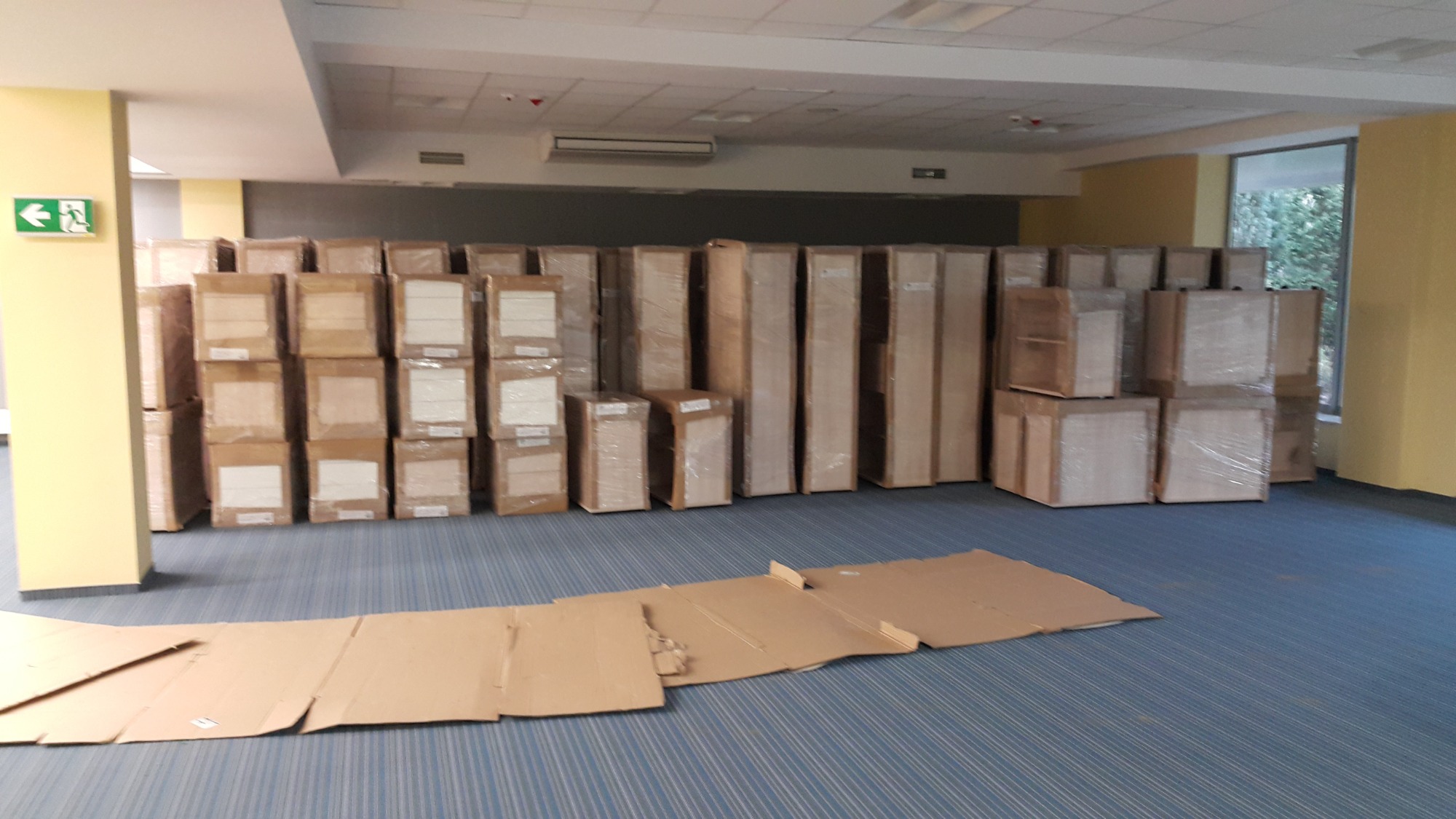 Meble zapakowane w folię i kartony, przygotowane do transportu, leżące na podłodze wyłożonej kartonami ochronnymi.