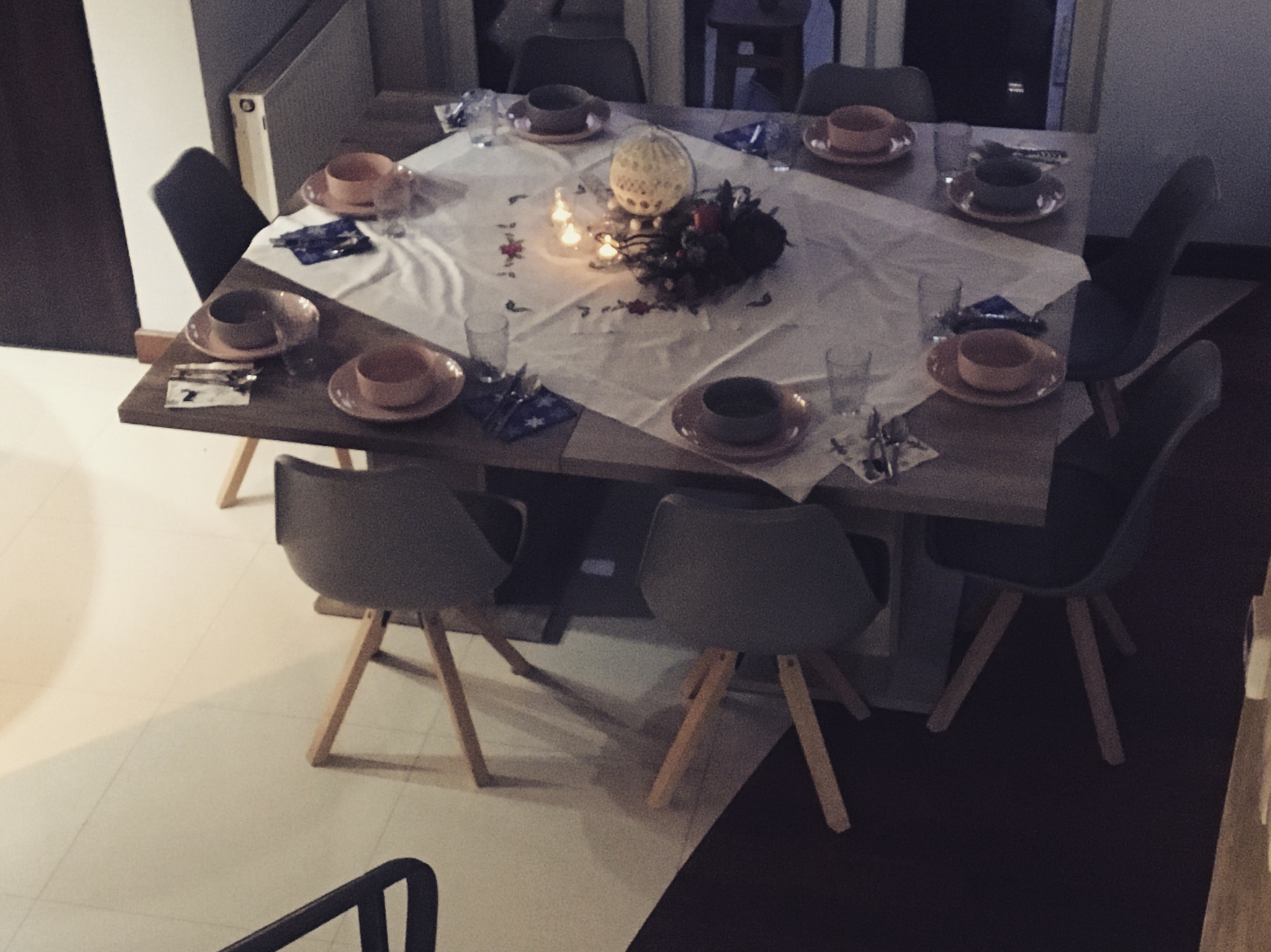 Stół jadalny z nakryciem dla wielu osób, dekorowany stroikiem świątecznym ze świecami i elementami roślinnymi, ustawiony w jasnym wnętrzu.