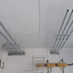 Montaż rur instalacji w nowym budynku w Lublinie, widoczne rury podwieszone do sufitu oraz fragment instalacji naściennej z zaworami i manometrami.