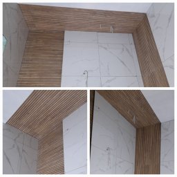 P.U.H.DortMet - Wnętrze łazienki w trakcie wykańczania: białe płytki imitujące marmur na ścianach, drewniane panele lamelowe na suficie i fragmencie ściany, widoczne przewody instalacji.