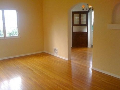 Pusty pokój z parkietem i żółtymi ścianami, widok na wnękę z zabudowaną szafą, okno po lewej stronie.