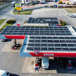 Widok z drona na stację benzynową Orlen z panelami słonecznymi na dachu, otoczoną parkingiem i drogą.