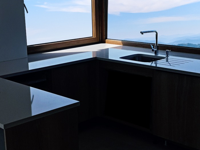 Kuchenny blat kamienny w odcieniach szarości, z widokiem na góry przez narożne okno, minimalistyczny design.