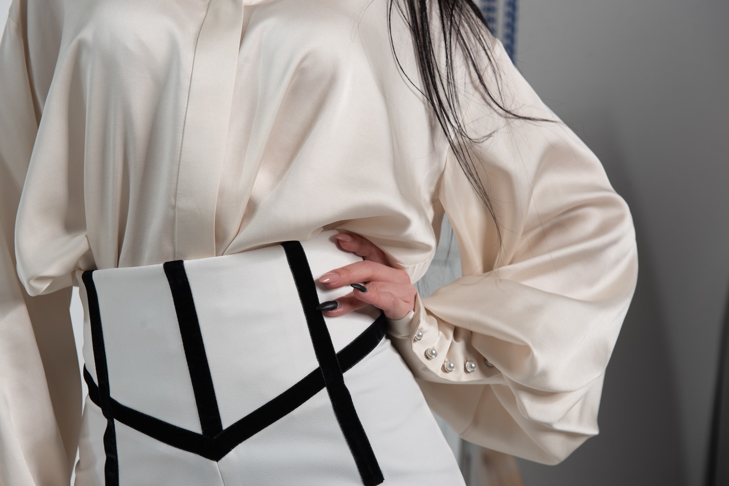 Kremowa, satynowa bluzka z bufkami i perłowymi guzikami na mankietach zestawiona z białą spódnicą z geometrycznym, czarnym zdobieniem.