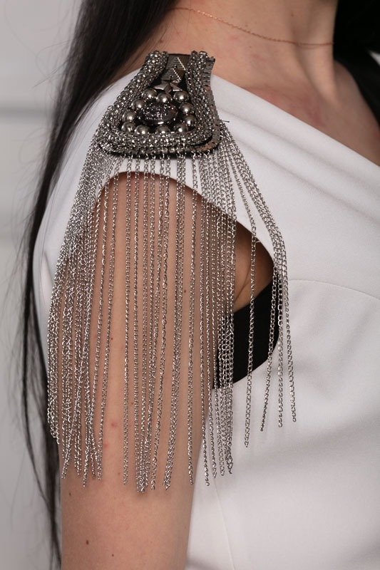 Biała sukienka z ozdobnym naramiennikiem z metalowymi koralikami i łańcuszkami, widok z bliska na ramię i dekolt.