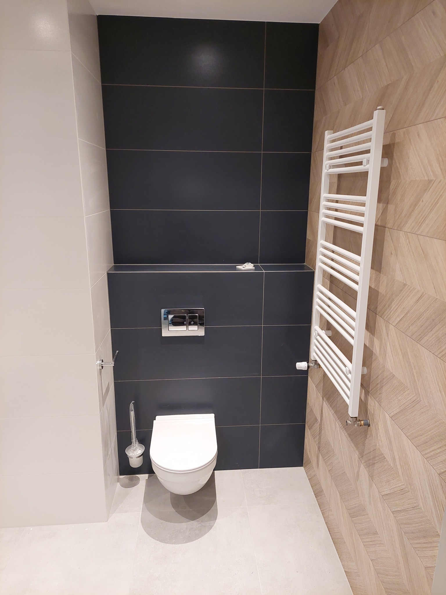 Nowoczesna toaleta z wiszącą muszlą, czarnymi kaflami, drewnopodobnymi panelami na ścianie i białym grzejnikiem drabinkowym.