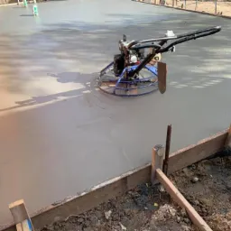 Wyrównywanie świeżo wylanego betonu na budowie przy użyciu zacieraczki mechanicznej, widoczne drewniane szalunki.