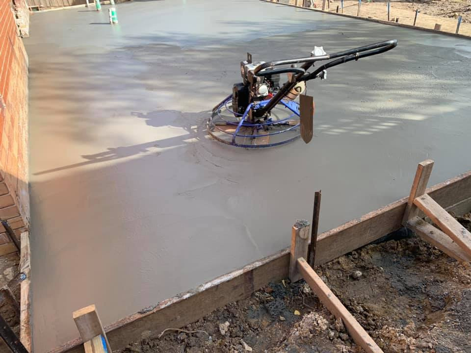 Wyrównywanie świeżo wylanego betonu na budowie przy użyciu zacieraczki mechanicznej, widoczne drewniane szalunki.