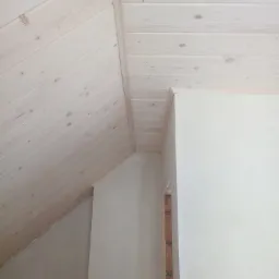 Jasne, pomalowane na biało deski boazeryjne na suficie i ścianie poddasza, widoczne surowe fragmenty muru.