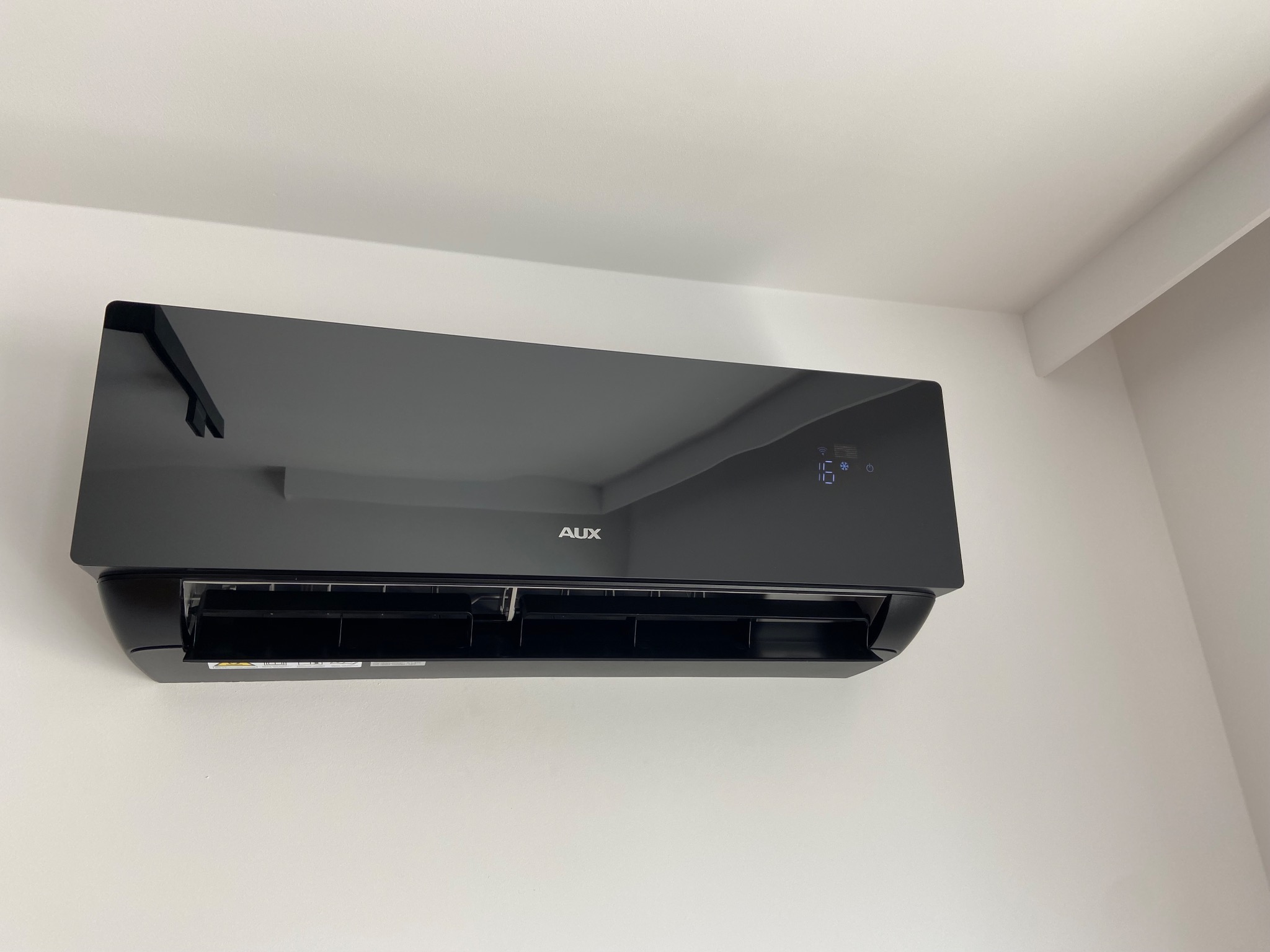 Czarny klimatyzator AUX J-Smart Art zamontowany na białej ścianie, wyświetlający temperaturę 16 stopni Celsjusza.