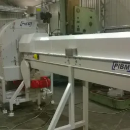 Biała, przemysłowa maszyna z elementami obróbki metalu, z widocznym logo PIBM, w tle inne maszyny w hali produkcyjnej.