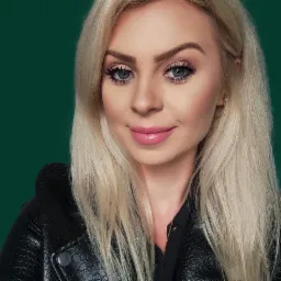 Portret uśmiechniętej blondynki w czarnej skórzanej kurtce na jednolitym ciemnozielonym tle, z delikatnym makijażem i złotymi kolczykami.