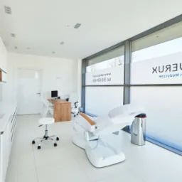 Jasne, minimalistyczne wnętrze gabinetu lekarskiego z białymi meblami, fotelem zabiegowym i dużym oknem z logo 'Severux Centrum Medyczne'.