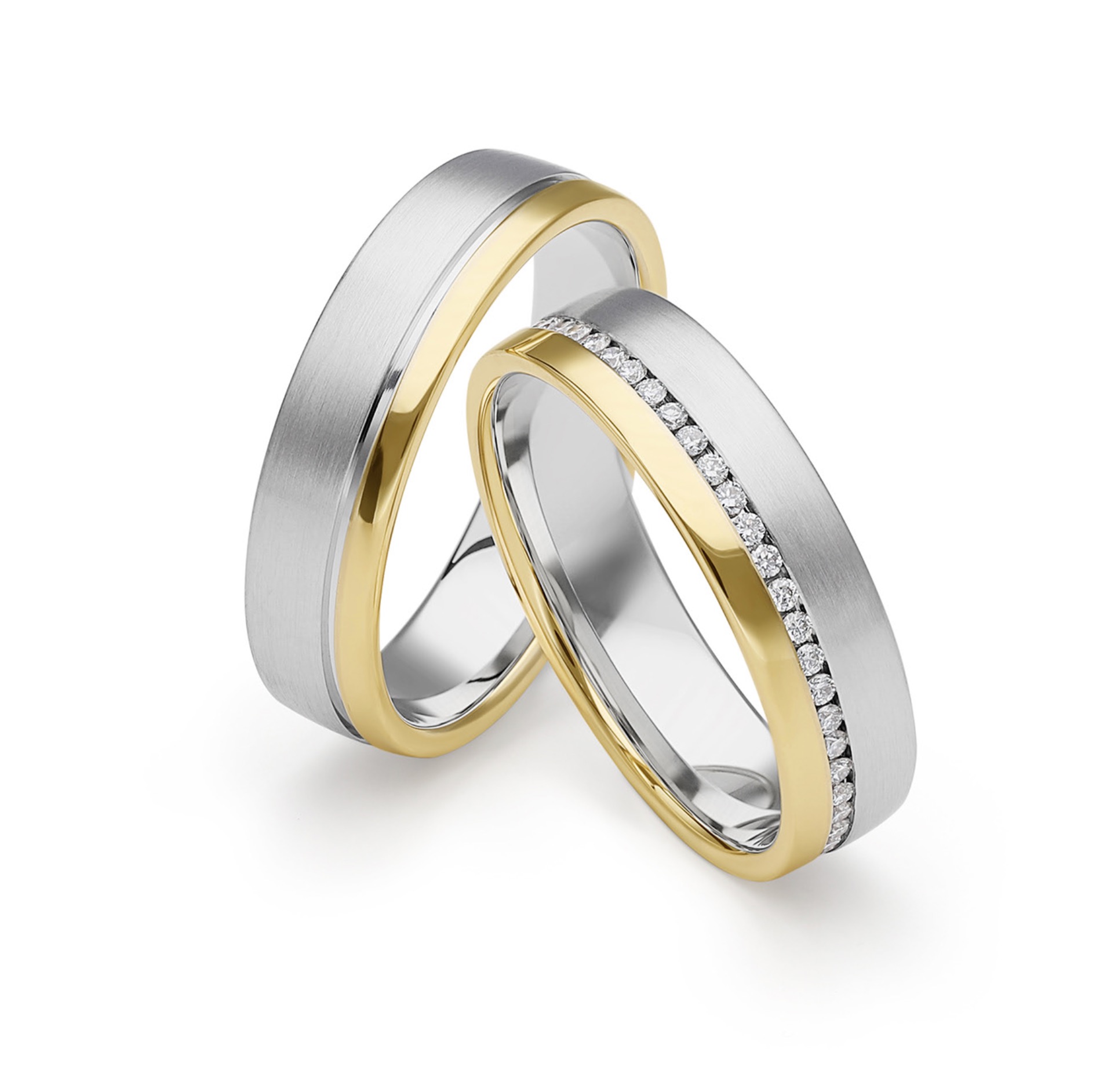 Dwie obrączki ślubne: jedna z matowego srebra z żółtym złotem i rzędem drobnych diamentów, druga z matowego srebra z żółtym złotem, leżące na białym tle.