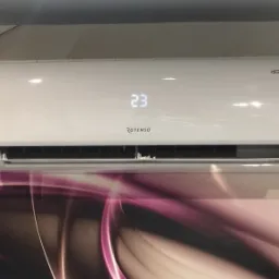 Biały klimatyzator Rotenso z wyświetlaczem temperatury 23 stopnie Celsjusza, zamontowany na ścianie z wzorem w odcieniach różu i fioletu.