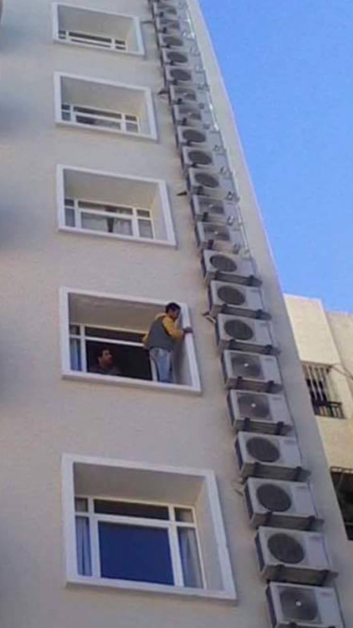 Elewacja budynku z rzędem zamontowanych klimatyzatorów, mężczyzna wyglądający przez okno, widok z dołu.