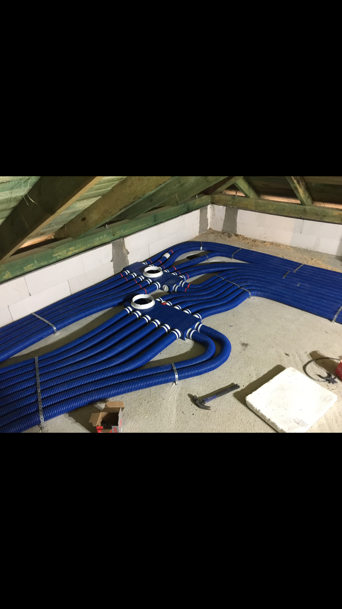 Niebieskie, karbowane rury wentylacyjne rozprowadzone na poddaszu, połączone białymi elementami, z widocznym młotkiem i pudełkiem narzędzi.