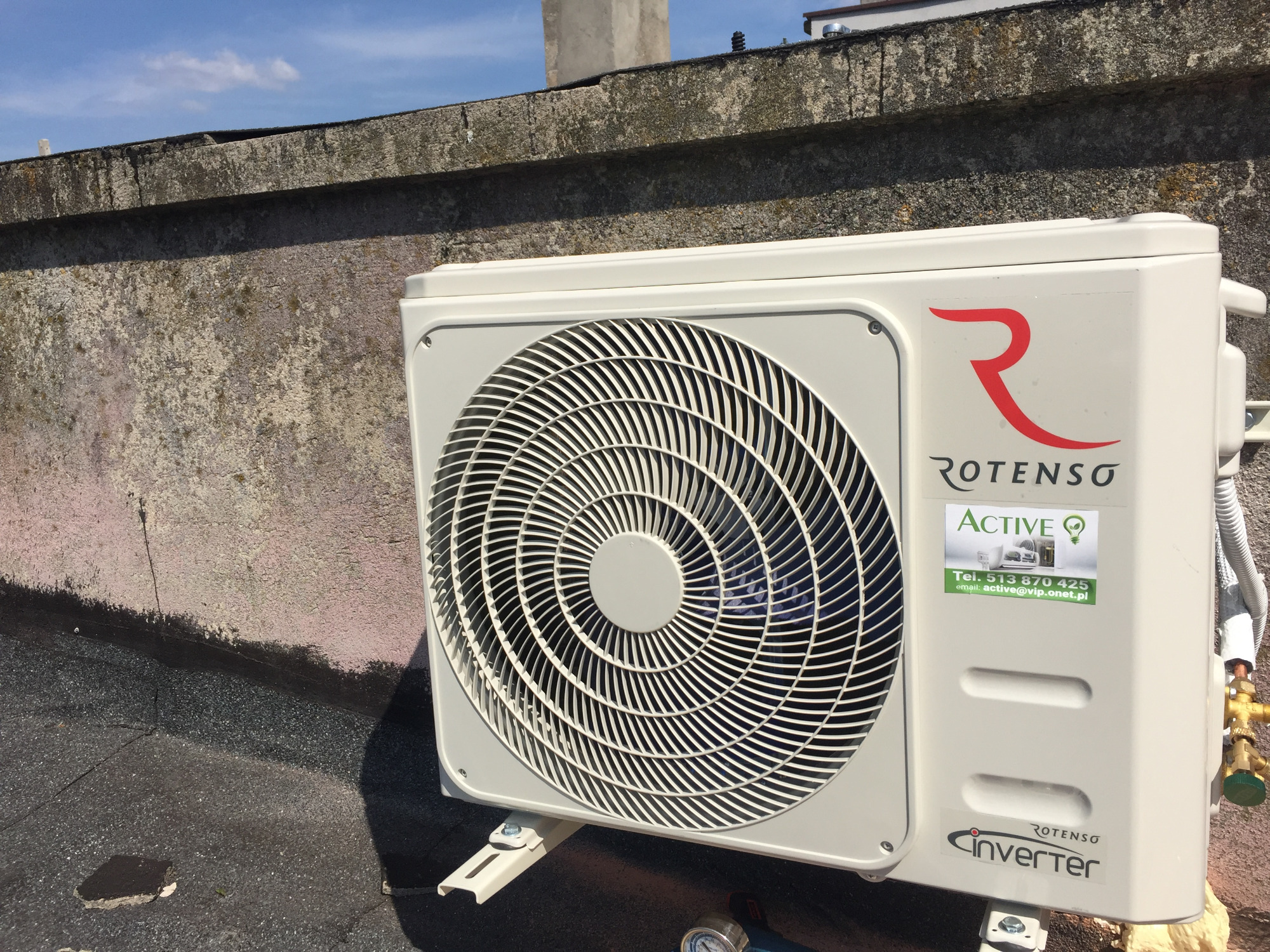 Zewnętrzna jednostka klimatyzacji Rotenso Inverter zamontowana na dachu budynku, widoczna naklejka z danymi kontaktowymi firmy Active.