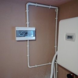 VESTIGO PC SPÓŁKA Z OGRANICZONĄ ODPOWIEDZIALNOŚCIĄ - Biała instalacja z rur PCV, skrzynka elektryczna i piec gazowy na beżowej ścianie w pomieszczeniu.