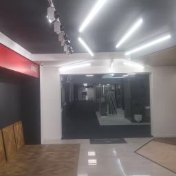 Firma remontowo budowlana Leszek Grabowski - Wnętrze salonu z ekspozycją paneli podłogowych z drewna w różnych wzorach i kolorach, oświetlenie sufitowe LED, widoczne logo 'Imperio Collection by Lareco'.