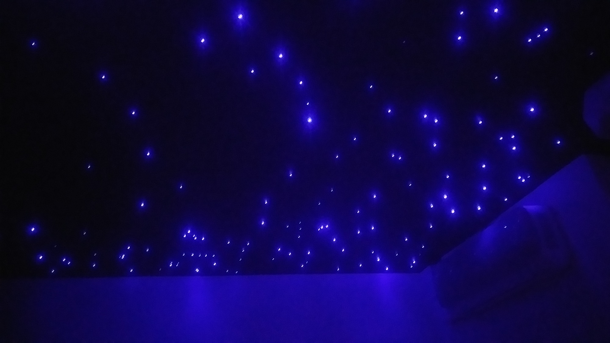 Nastrojowy sufit z punktowymi, niebieskimi diodami LED imitującymi rozgwieżdżone niebo, widoczne fragmenty ściany i podłogi w ciemnym odcieniu niebieskiego.