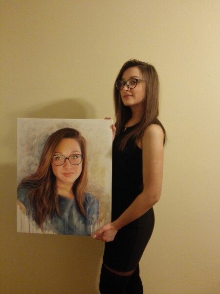 Młoda kobieta w czarnej sukience trzyma portret olejny przedstawiający ją samą w okularach, format 50/60.