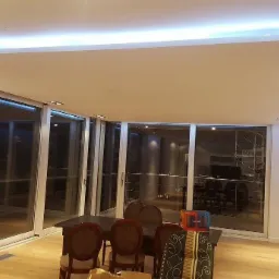 Nowoczesny salon z podwieszanym sufitem z oświetleniem LED, widoczne duże okna przesuwne i drewniana podłoga