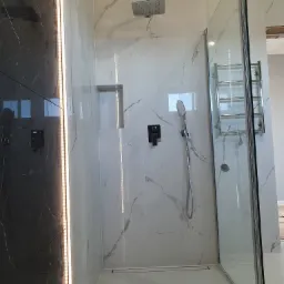 Nowoczesna kabina prysznicowa z czarną armaturą, wykończona płytkami imitującymi marmur, z oświetleniem LED wzdłuż ściany.