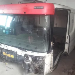 Częściowo zdemontowana kabina ciężarówki Scania z widocznymi elementami zawieszenia i silnika, czerwony dach kabiny, widoczne wnętrze kabiny.